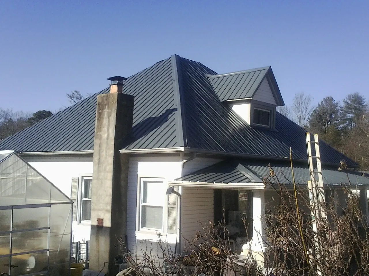 Dark blue standing seam metal roof on a white farmhouse with dormer — Slate & Tile Roof Repair by Roofing Brothers in New Millport
