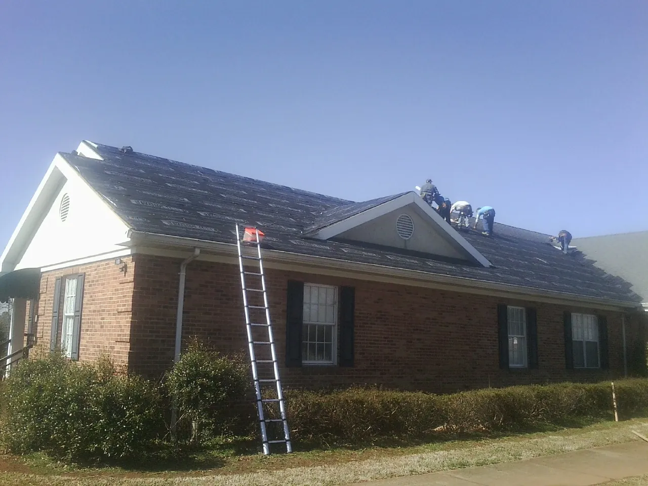 Crew tearing shingles off a brick ranch roof with a ladder set — Emergency Roof Repair work by our crew in New Millport