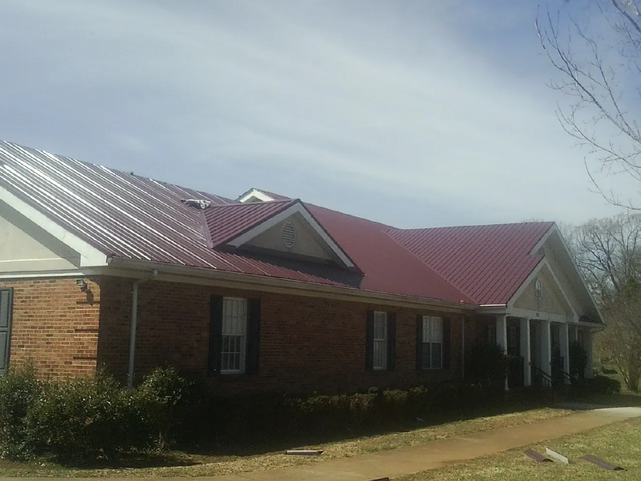 Red metal roof with gabled entries on a long brick building, from a Hail Damage Roof Repair job in New Millport