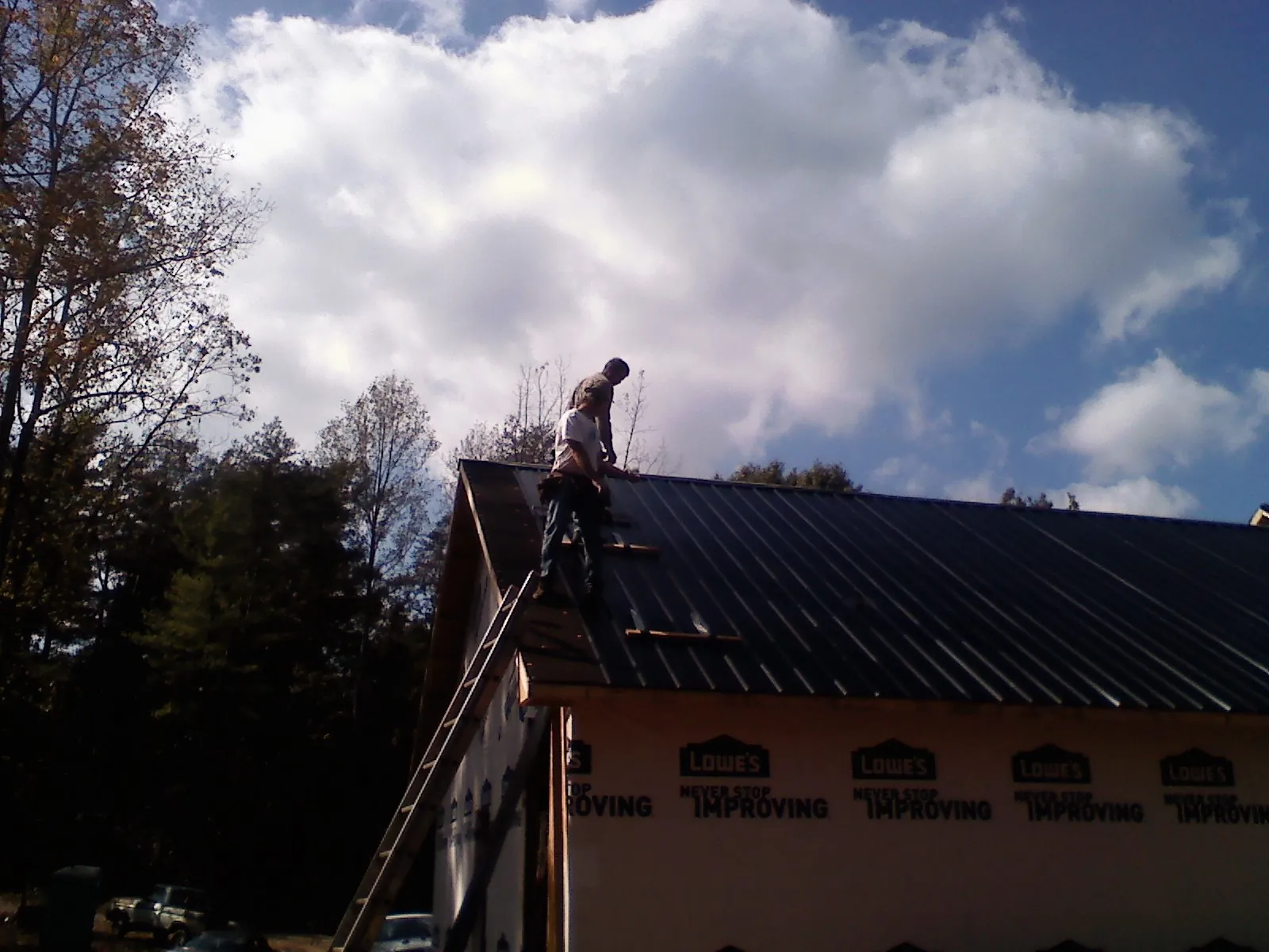 Roofer fastening dark metal panels high against a cloudy sky, from a Roof Inspection job in New Millport