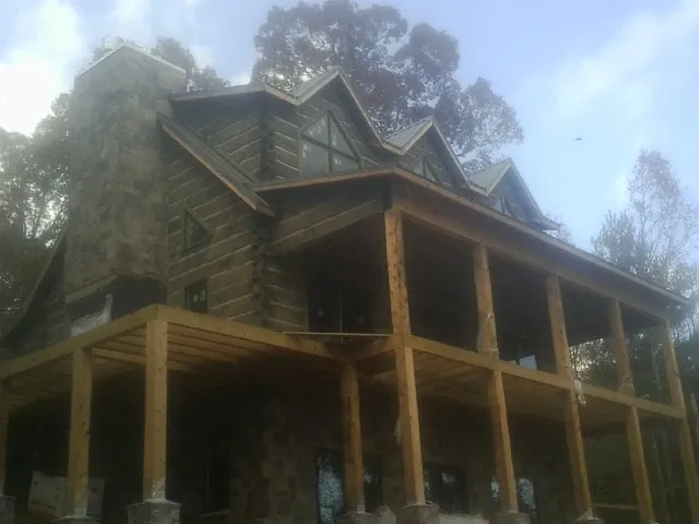 Stone chimney and dormers on a large log home with a timber porch in New Millport