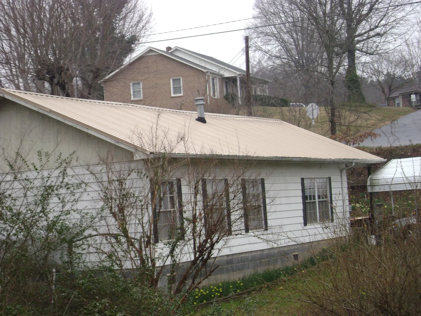 Tan metal roof on a white sided house set into a hillside — Commercial Roofing by Roofing Brothers in New Millport